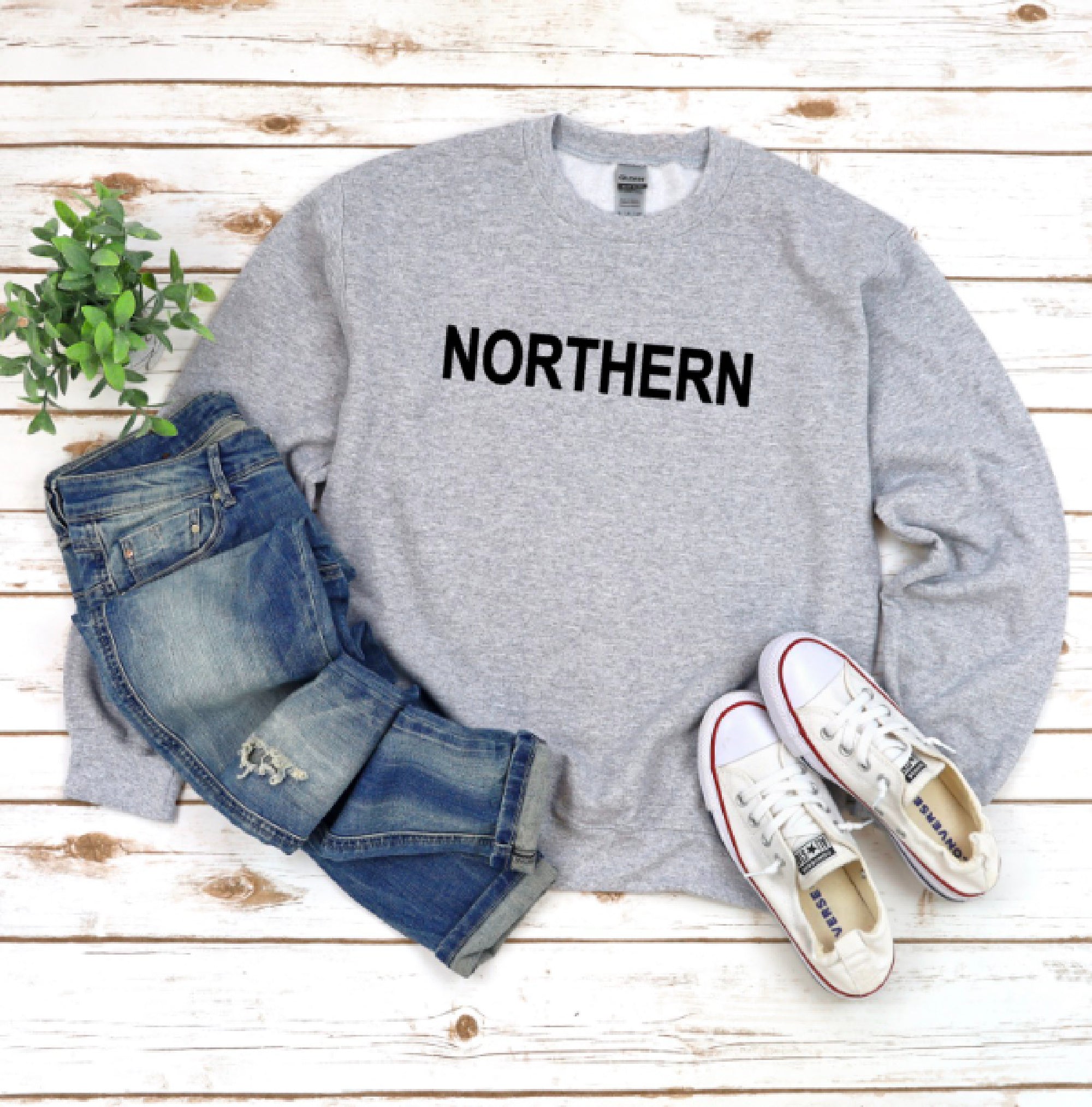 Gray sweatshirt with 'NORTHERN' text, blue jeans, and white sneakers on a wooden surface.