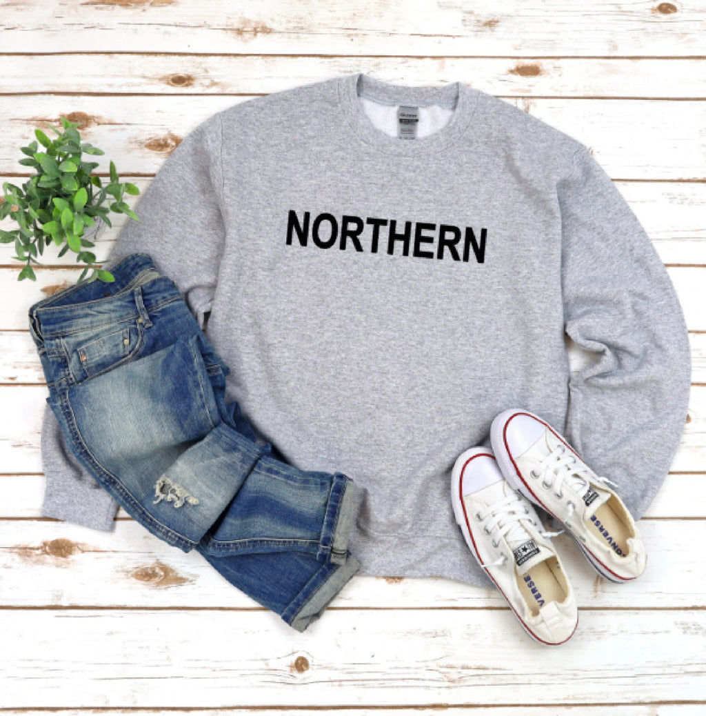 Gray sweatshirt with 'NORTHERN' text, blue jeans, and white sneakers on a wooden surface.